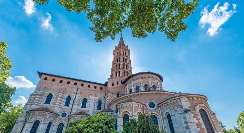 A pink and white church with an ornate steeple is backlit by the sun on a blue-sky day.