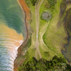 Dominical, Costa Rica - An aerial view of a car driving along a dirt road surrounded by water on either side. © Jordan Siemens / Getty Images
