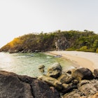 Butterfly Island: a crescent of beach with a single canoe moored on the sand, two more canoes are in the sea approaching the beach. Behind the beach is dense jungle.