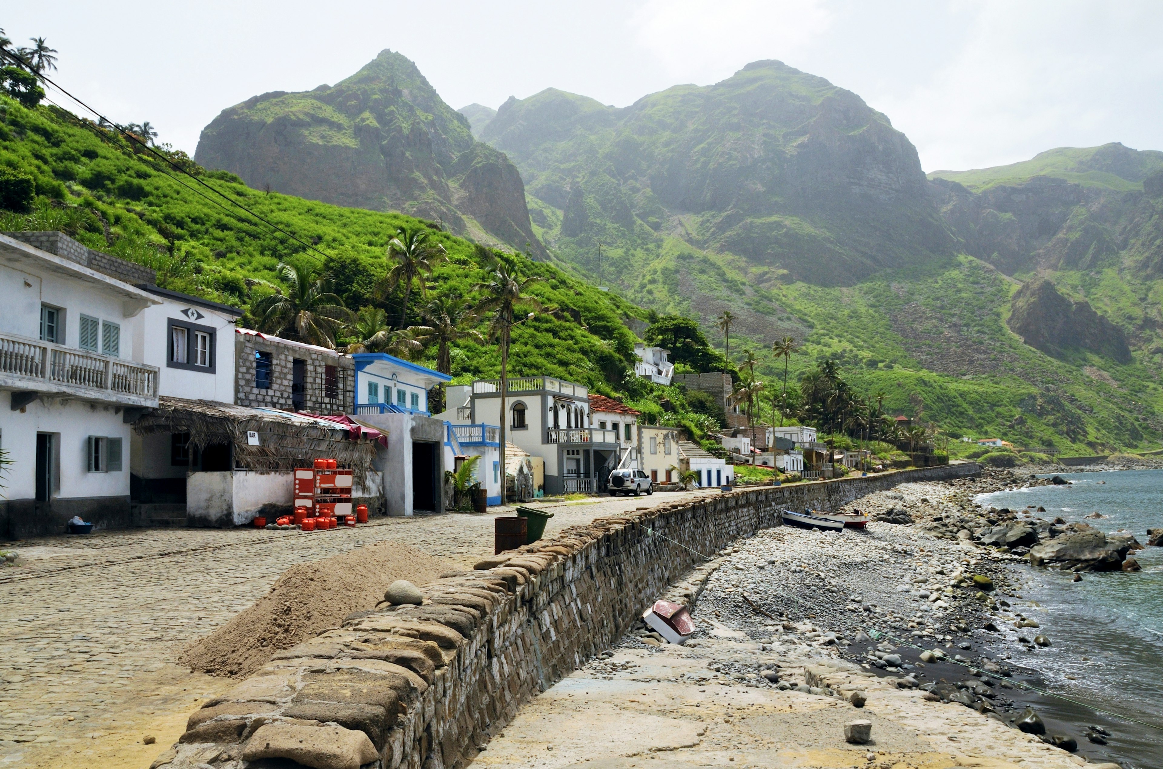 Homes and business line the oceanfront cobblestone street with lush mountains rising behind