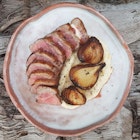 A close up of a plate of sliced meat with charred onion on a bed of white sauce