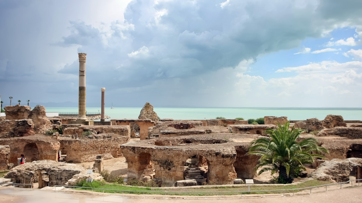 The image looks across a series of thick stone arches and two stone columns towards the sea, which has a thick thunder cloud over it.